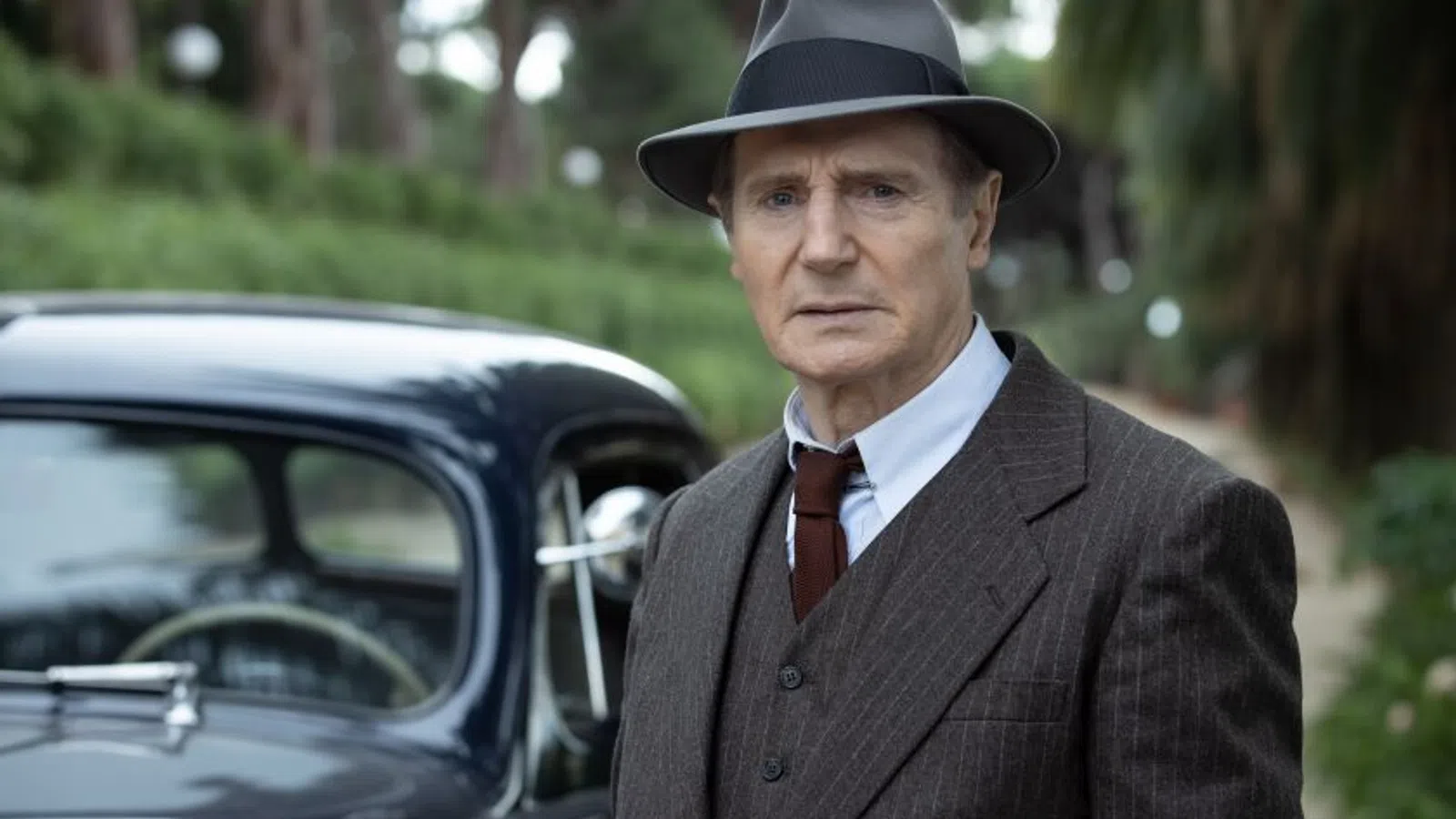 Liam Neeson in a suit and hat