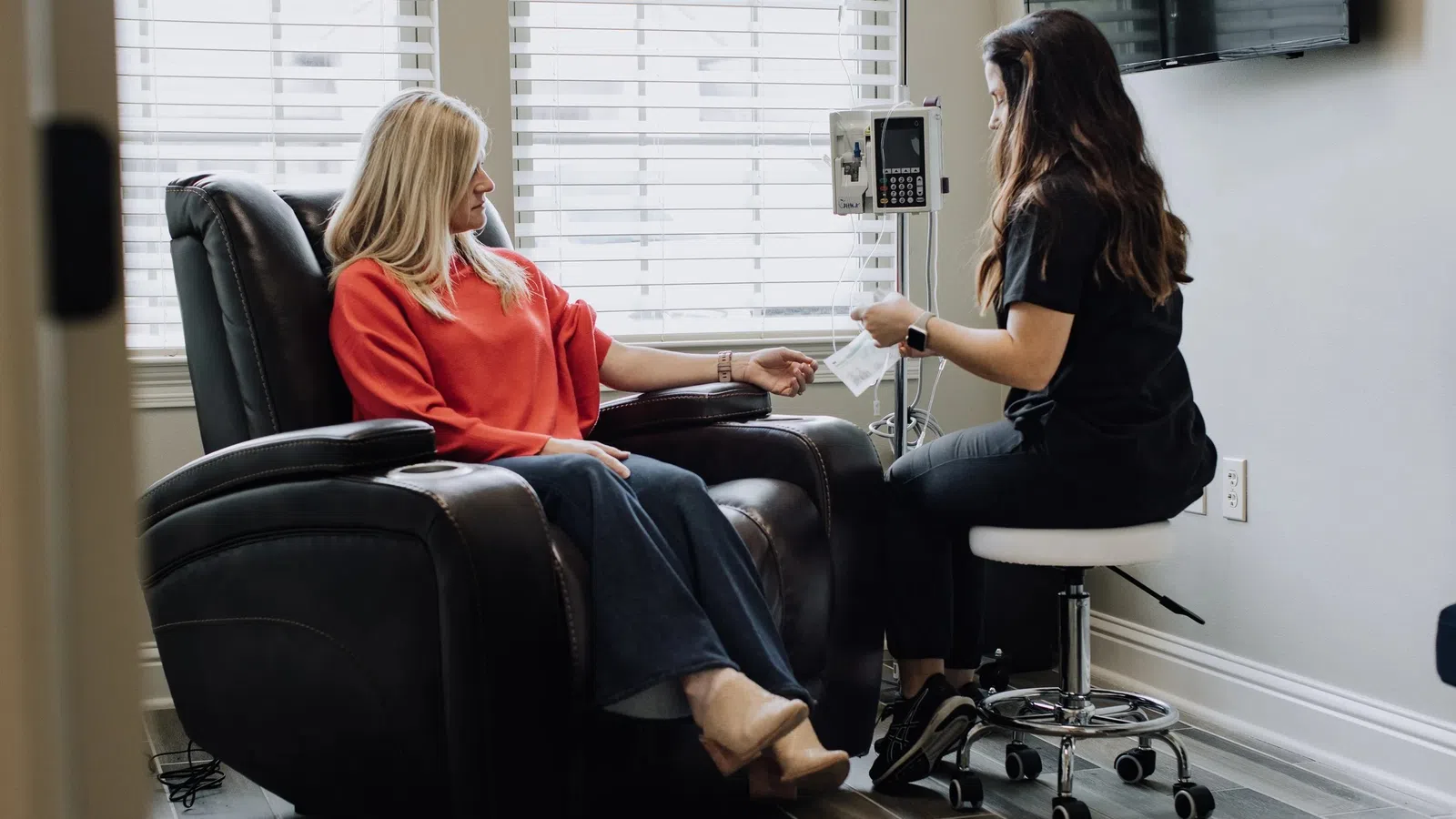 Woman in red sweater receiving intravenous treatment from healthcare professional in medical clinic.