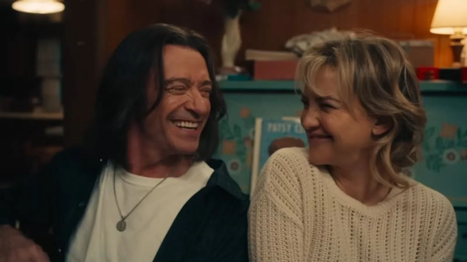Man and woman smiling warmly at each other in a cozy indoor setting with soft lighting.
