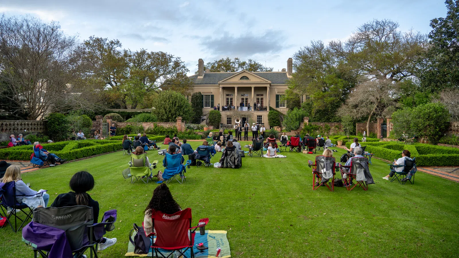 a group of people sitting in chairs in a grassy area with a building in the background