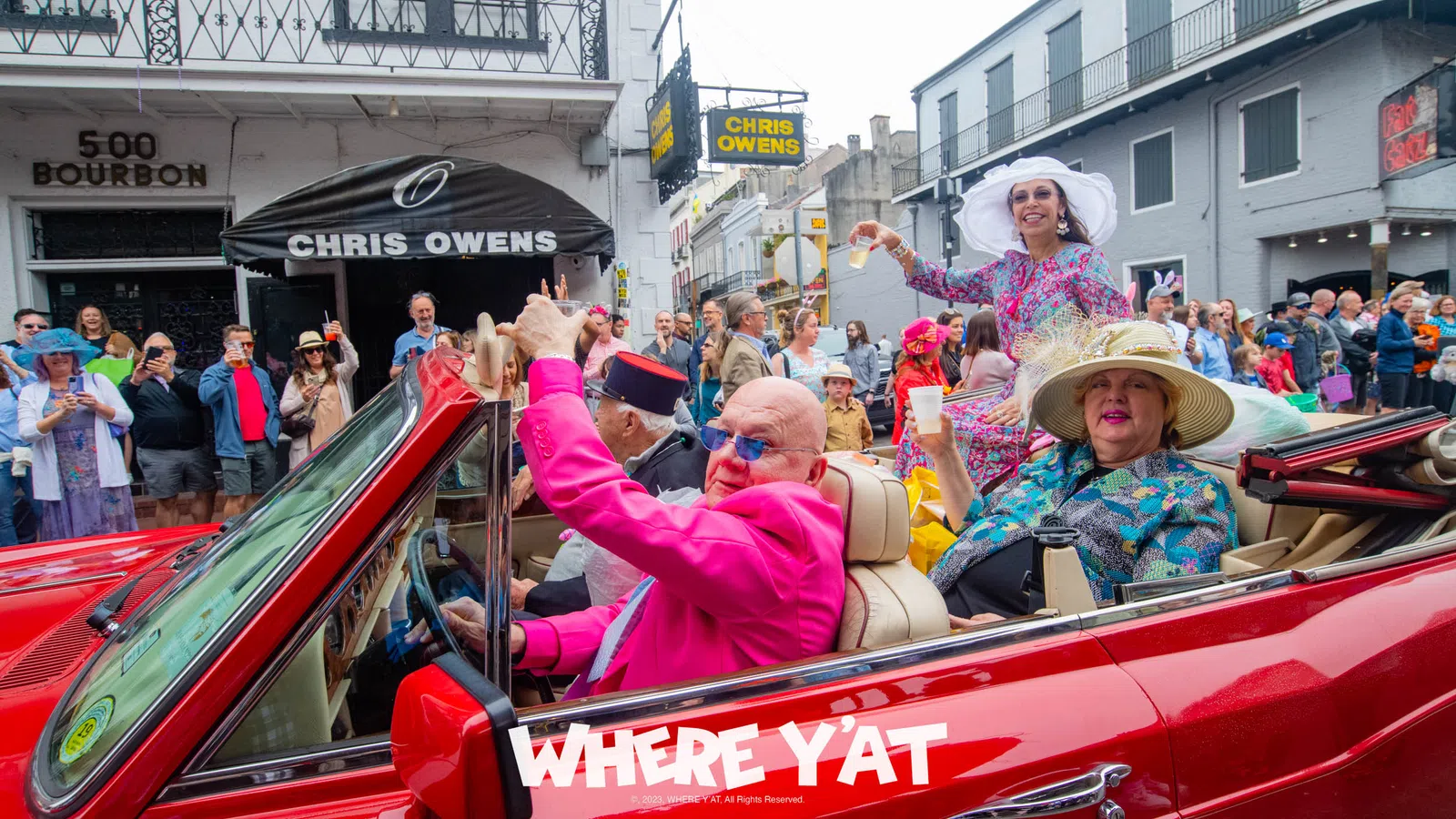 a group of people in a red car with a crowd watching