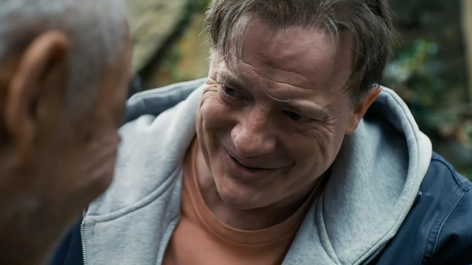 Middle-aged man smiling warmly at an elderly man in an outdoor setting with blurred natural background