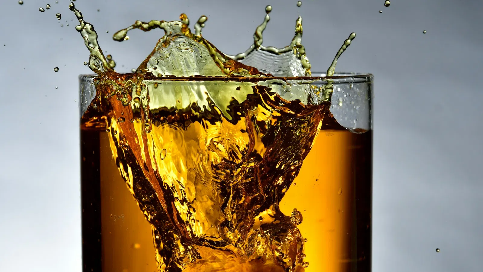 Close-up of a splash in a glass of dark liquid with ice cubes against a gray background