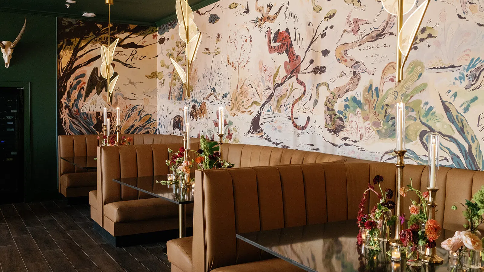 Cozy restaurant booths with floral arrangements and artistic mural on wall under modern gold pendant lights.
