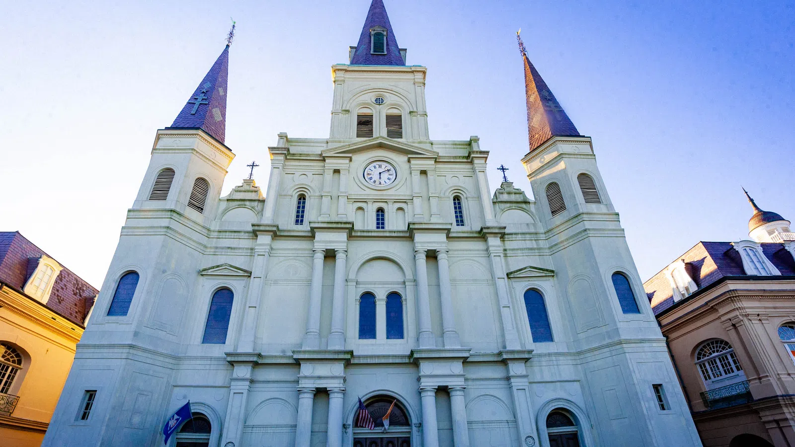 Front view of St. Louis Cathedral with three spires and clock, under clear blue sky at sunset.