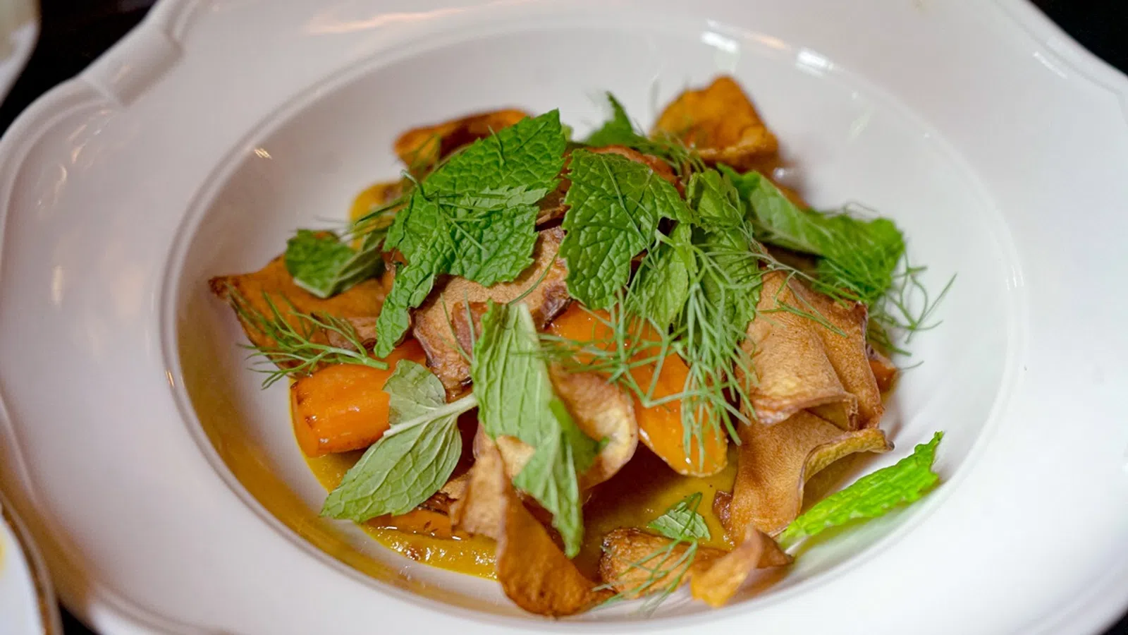 A gourmet dish with crispy vegetables and fresh herbs served in a white bowl.