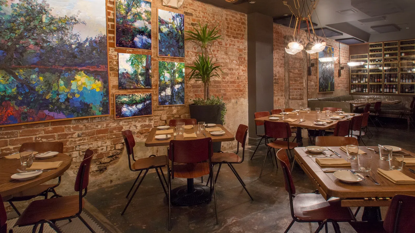 Cozy restaurant interior with wooden tables, colorful abstract art on brick walls, and modern lighting fixtures.