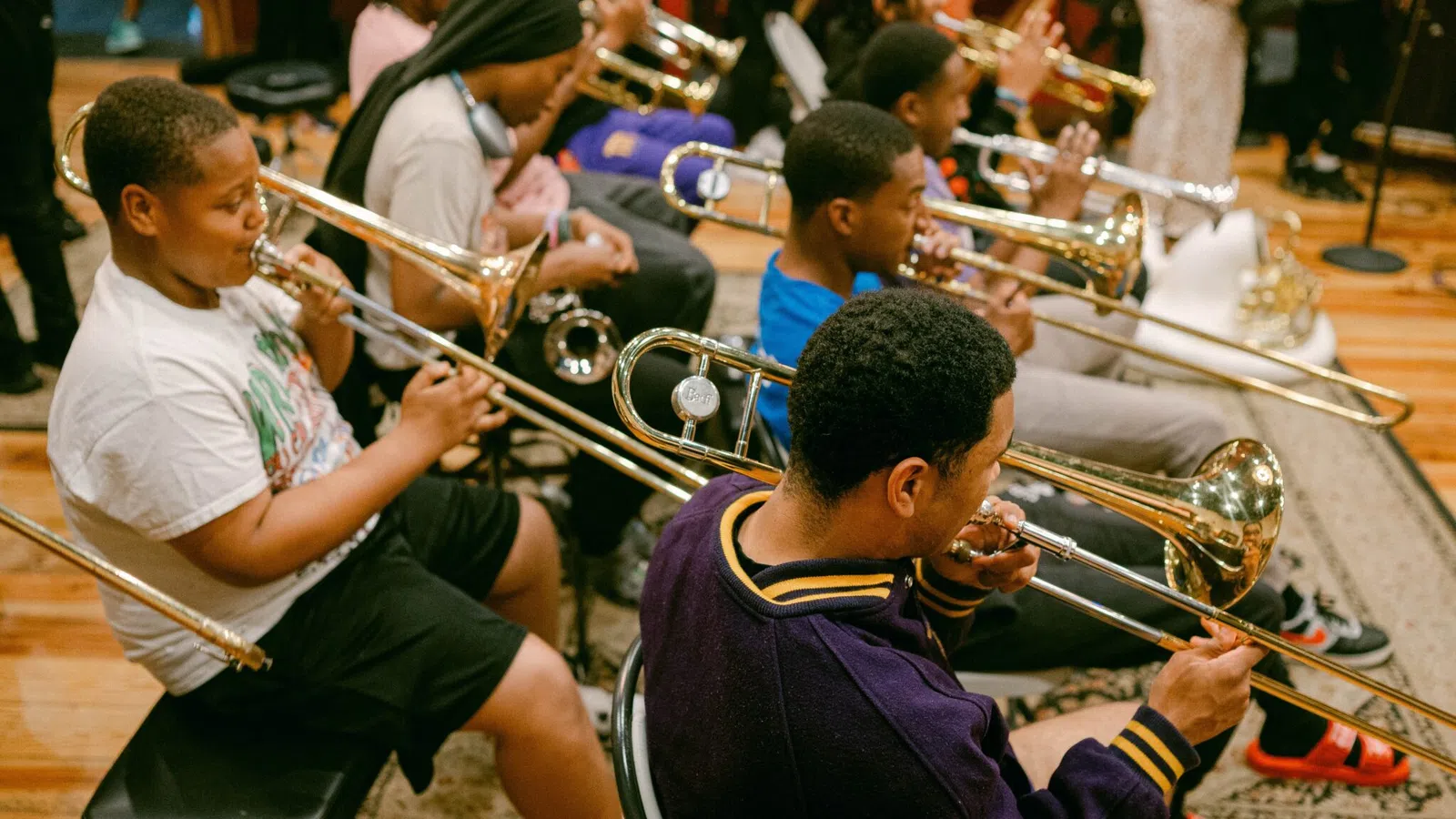 Young musicians playing trombones in a group rehearsal inside a music studio with wooden floors.