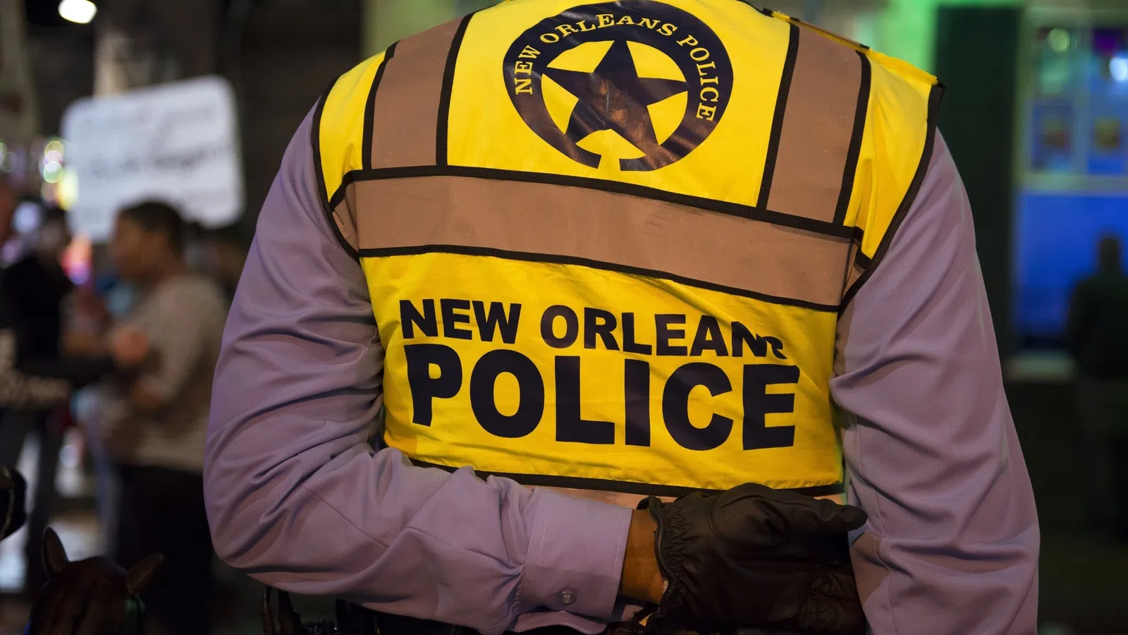 Back view of New Orleans police officer wearing a yellow reflective vest during nighttime patrol.