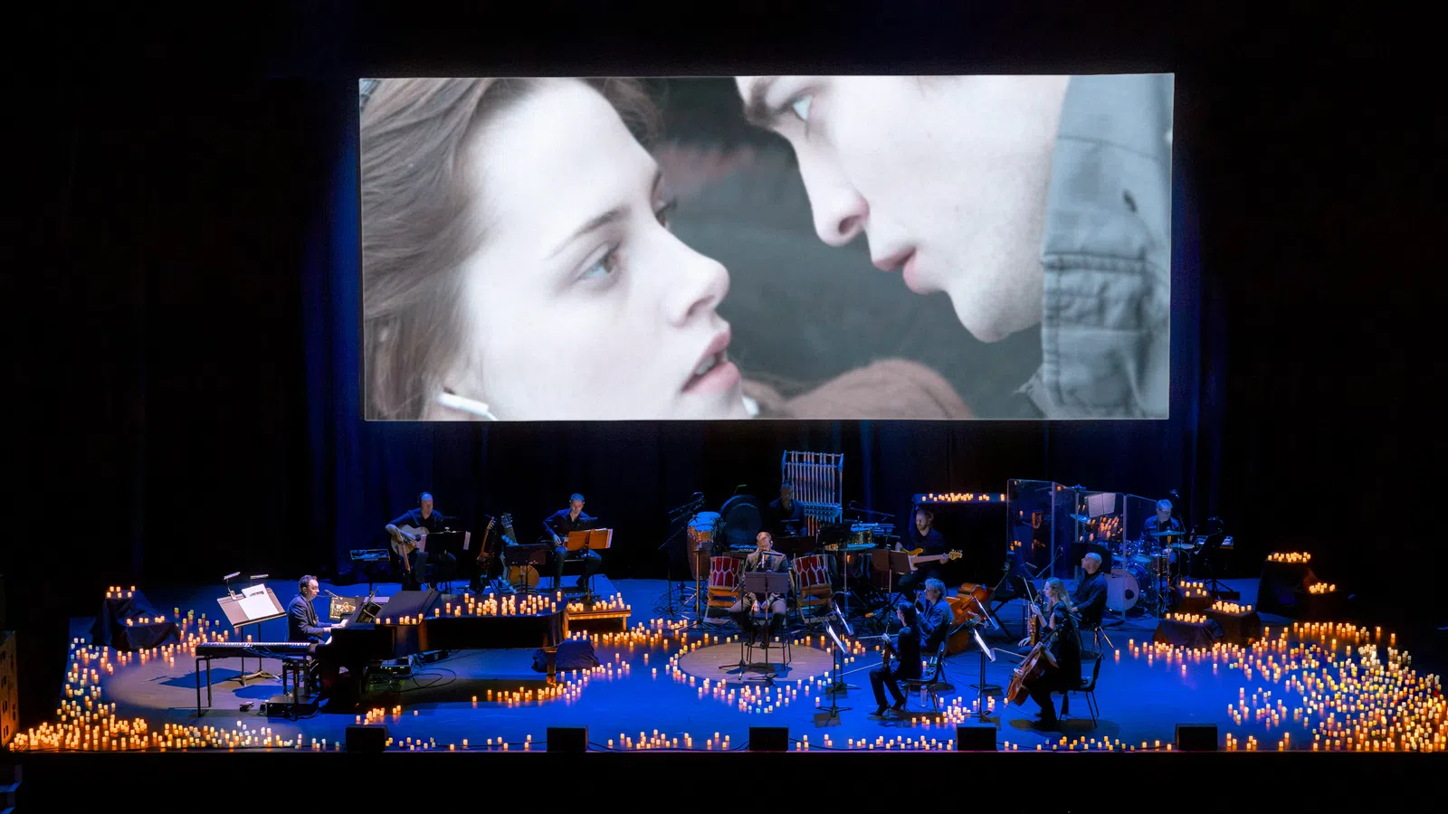 A live performance featuring musicians and a large screen displaying a romantic scene.