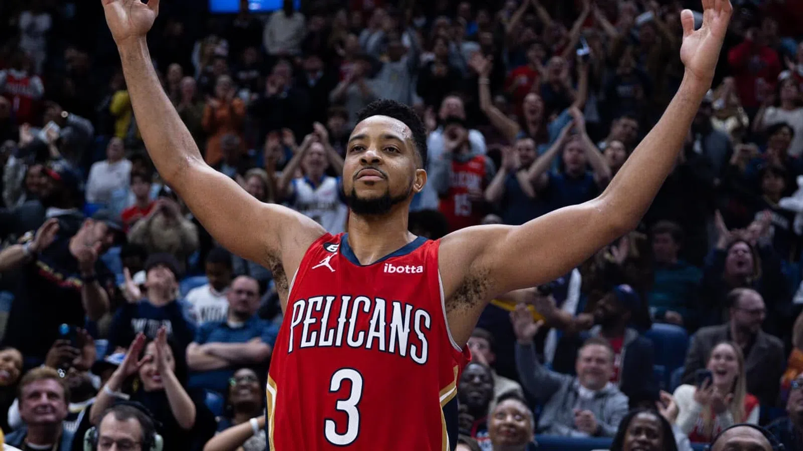 C.J. McCollum in a basketball uniform with his arms raised in front of a crowd