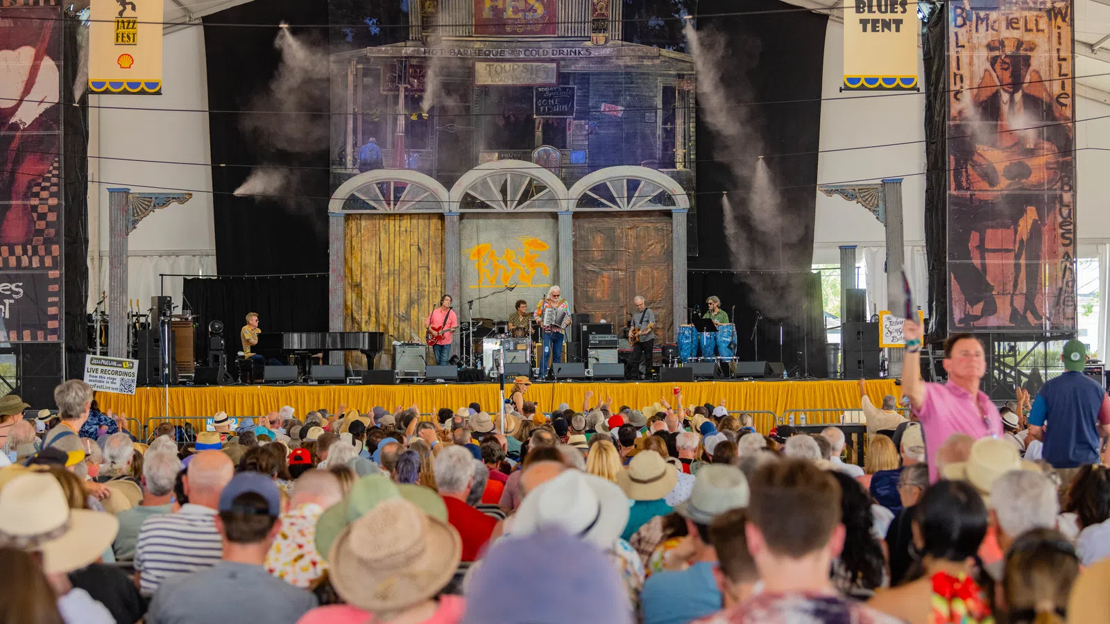 A lively music performance on stage at a festival, with a large audience enjoying the show.