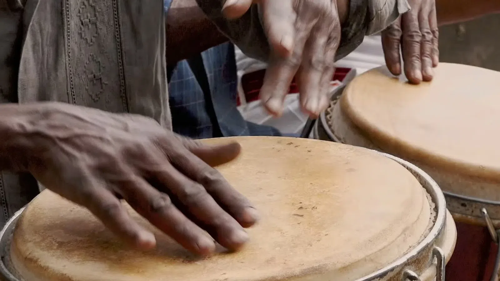 Close-up of hands playing traditional drums with textured beige drumheads in a lively setting