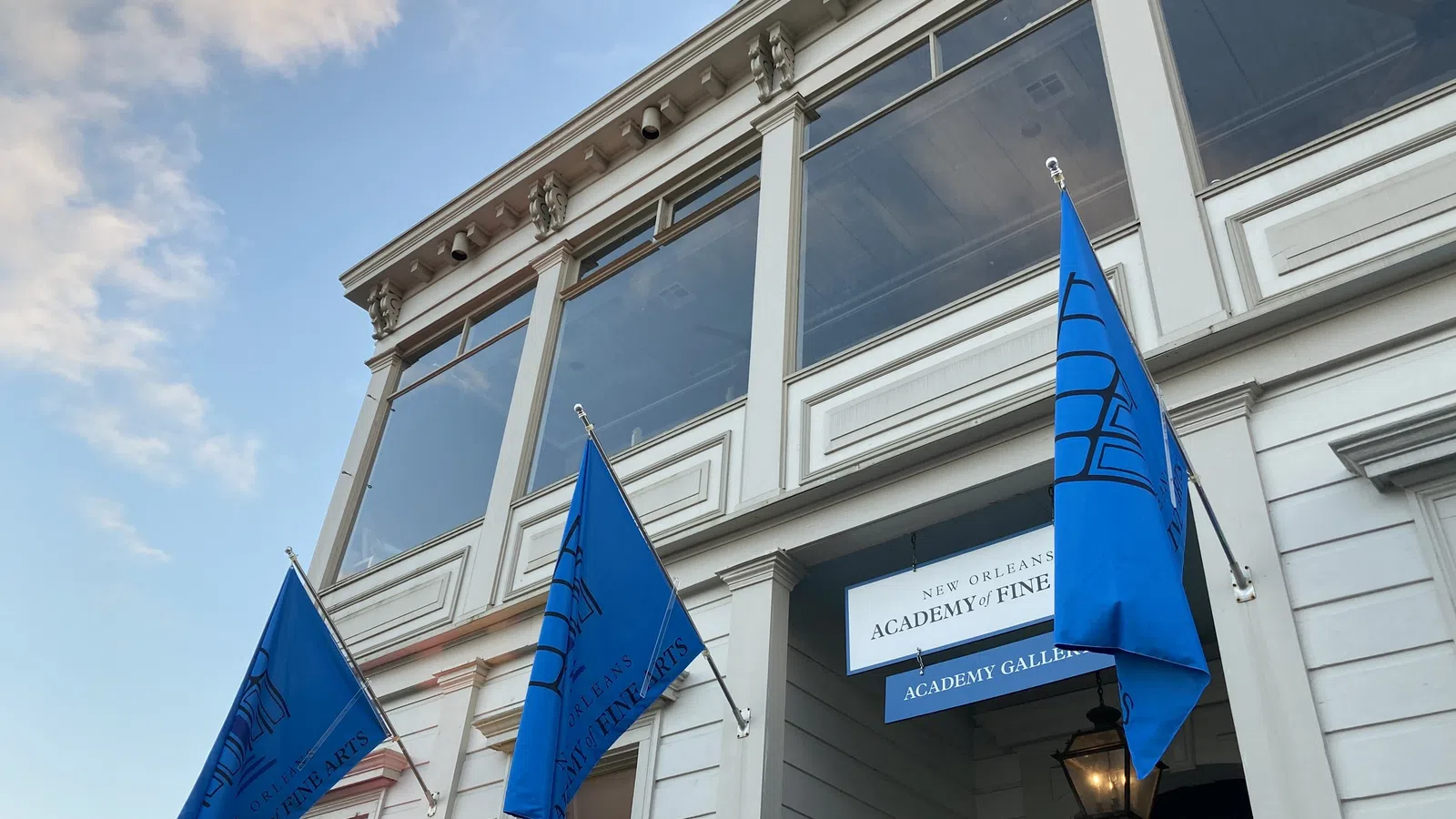 Exterior view of New Orleans Academy of Fine Arts with blue flags and clear sky at dusk