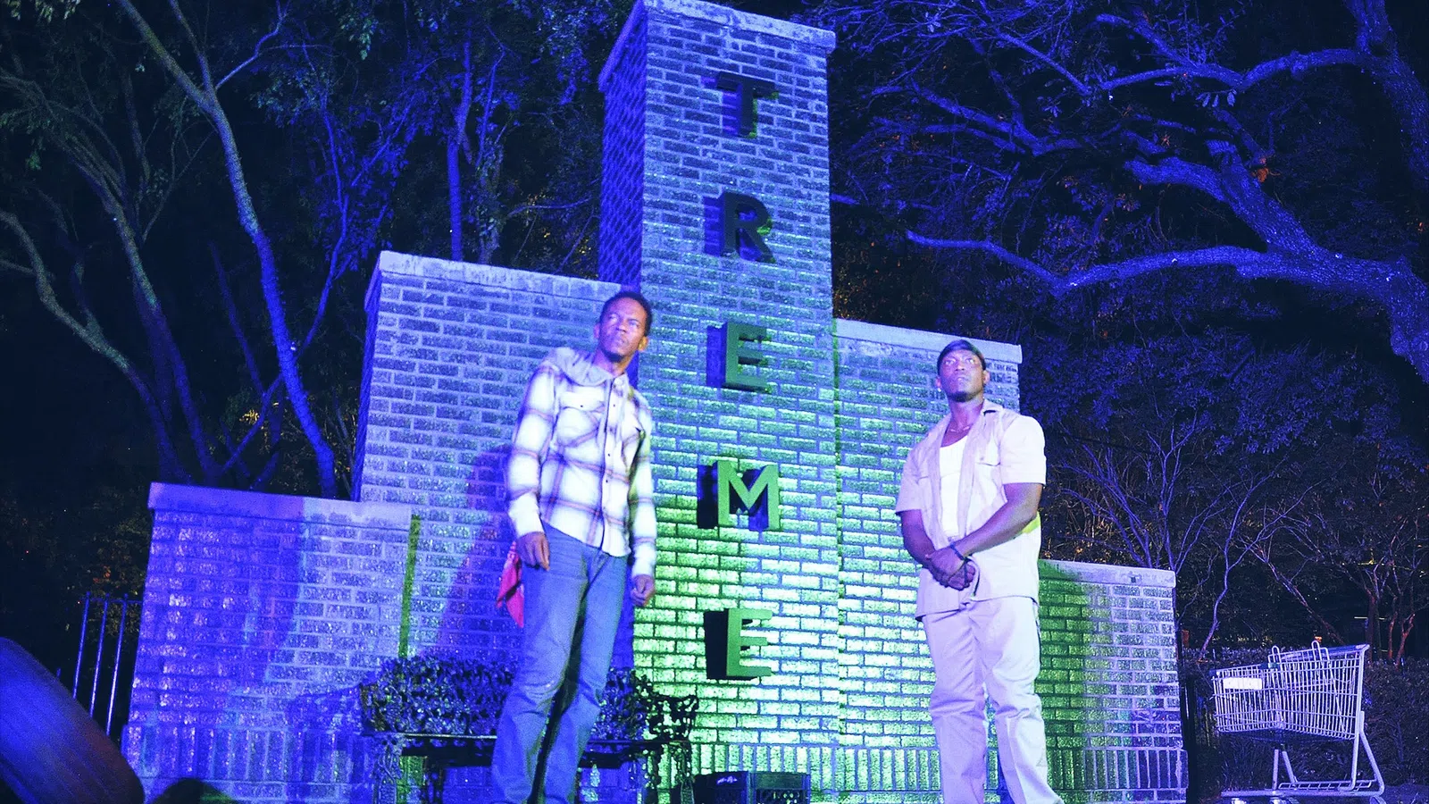 two men standing in front of a building with a fence and trees