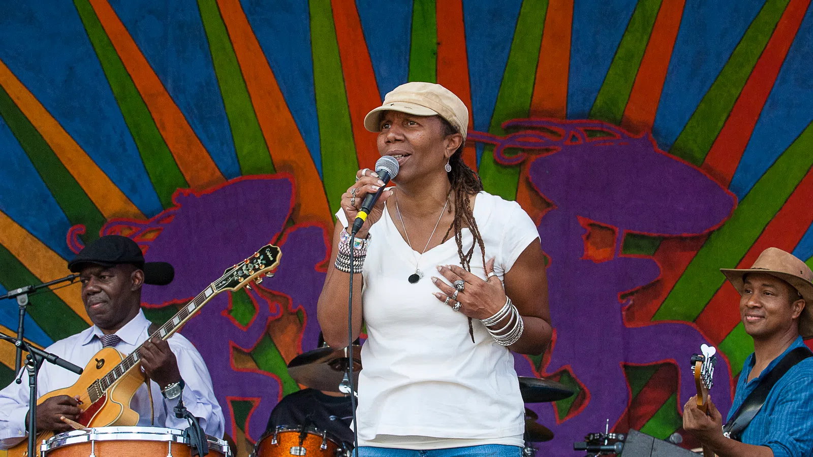 Female vocalist singing on stage with band members playing guitar and drums against vibrant backdrop