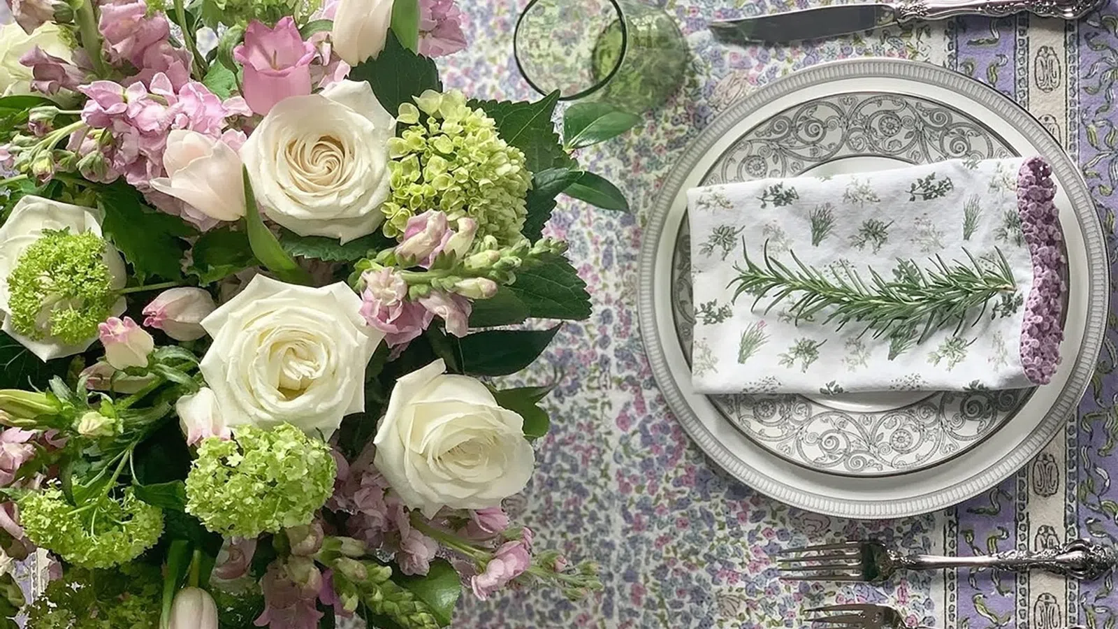Elegant floral centerpiece with white roses and green hydrangeas beside a lavender-themed place setting with a rosemary napkin.
