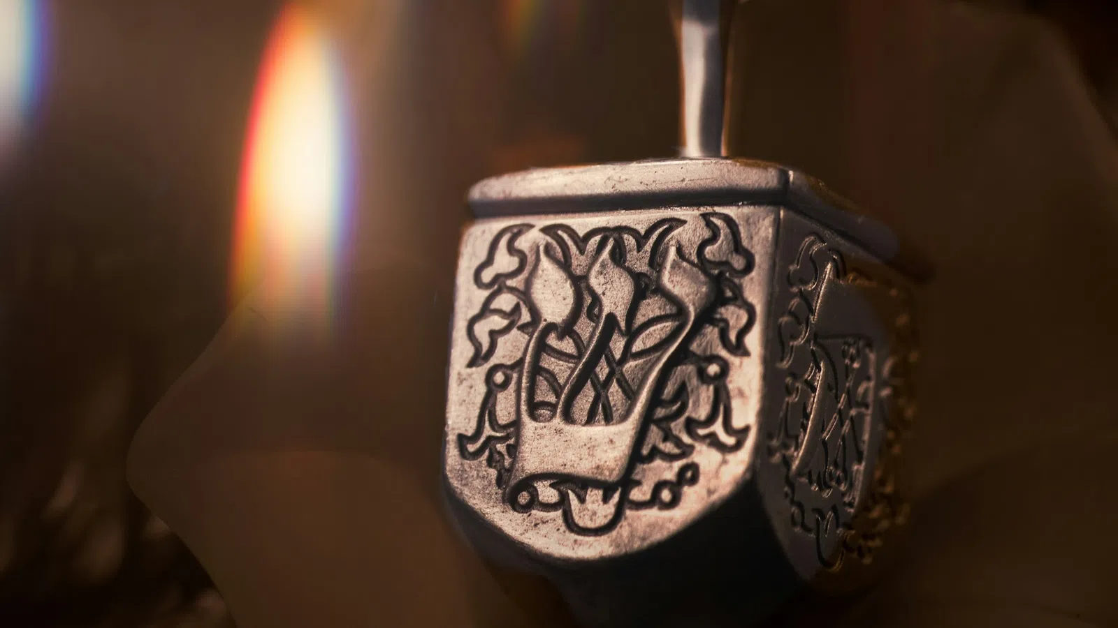 Close-up of a silver decorative dreidel with intricate Hebrew engravings and soft warm lighting.