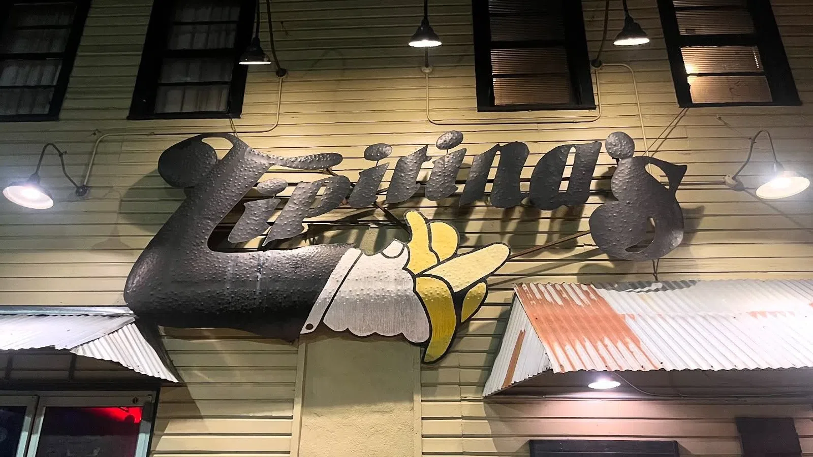 Sign for Lipiting's with a large pointing hand, mounted on a yellow wooden building under night lights.