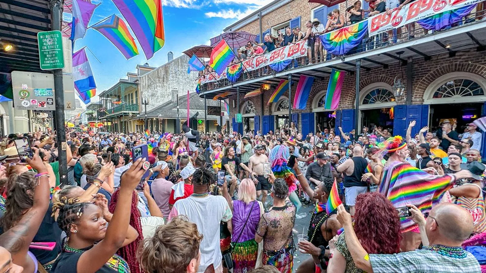 Crowd celebrating at a vibrant Pride parade with rainbow flags, colorful outfits, and lively street atmosphere.