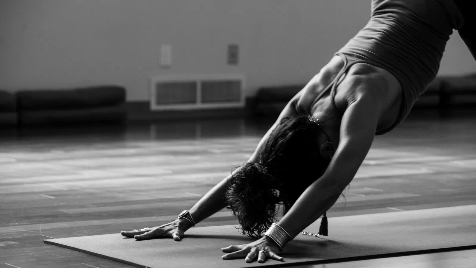 Woman practicing yoga in downward dog pose on a mat in a spacious studio with wooden floor.
