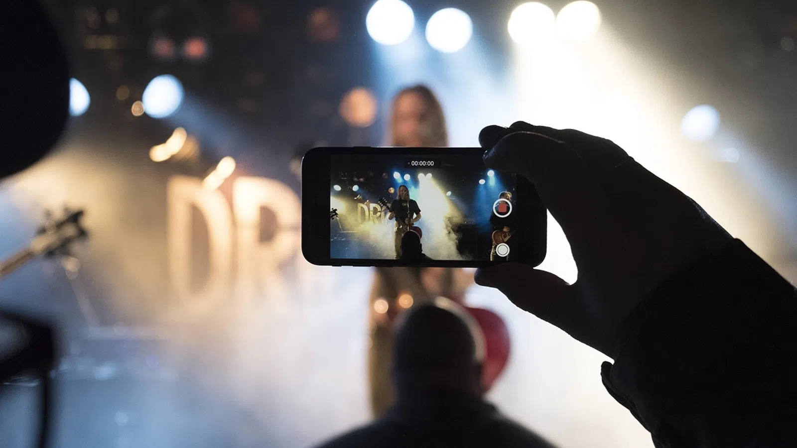 Person recording a live music performance on smartphone with stage lights and smoke effects in background