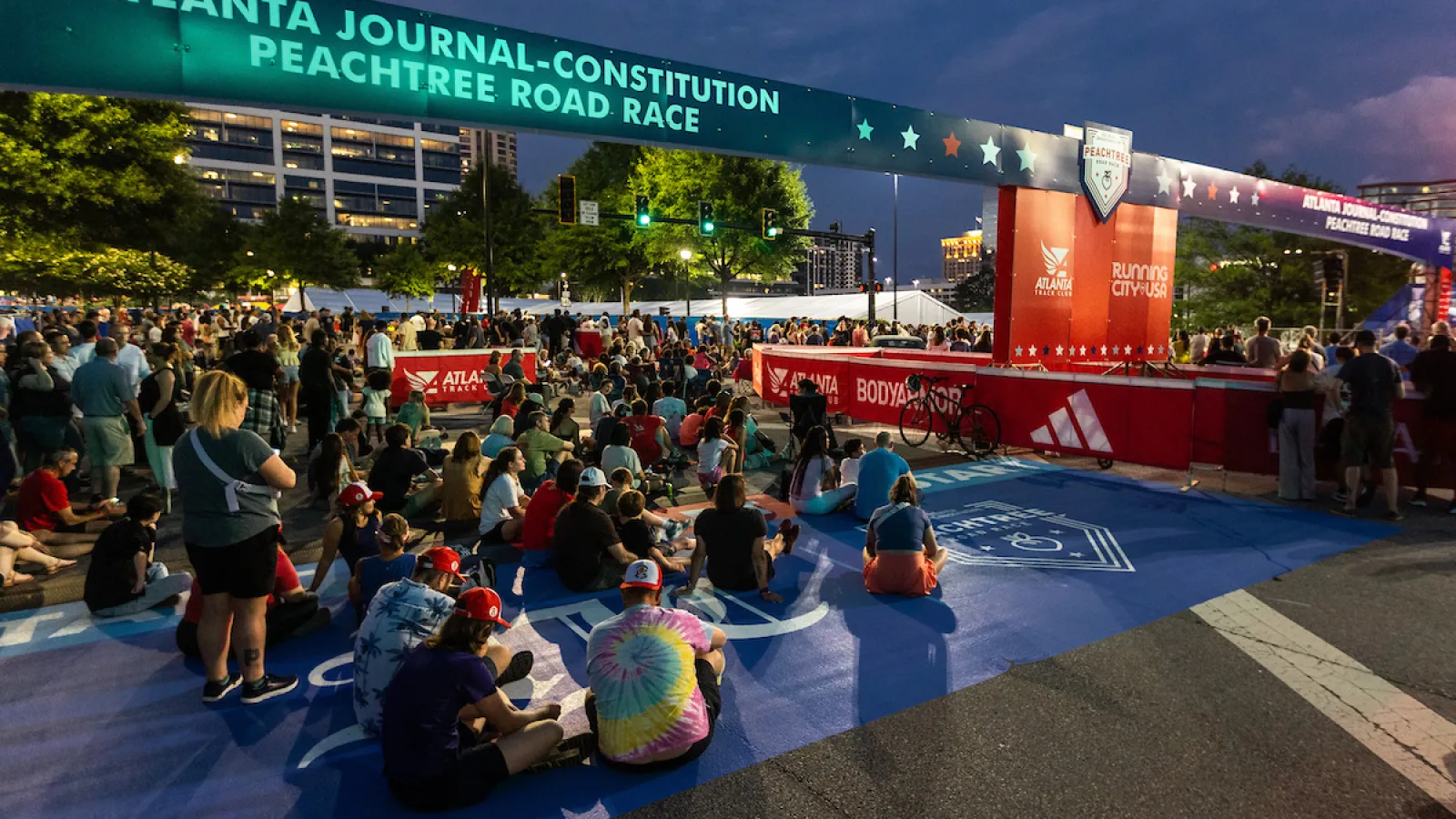 Crowd gathered under the Atlanta Journal-Constitution Peachtree Road Race start line banner at dusk.