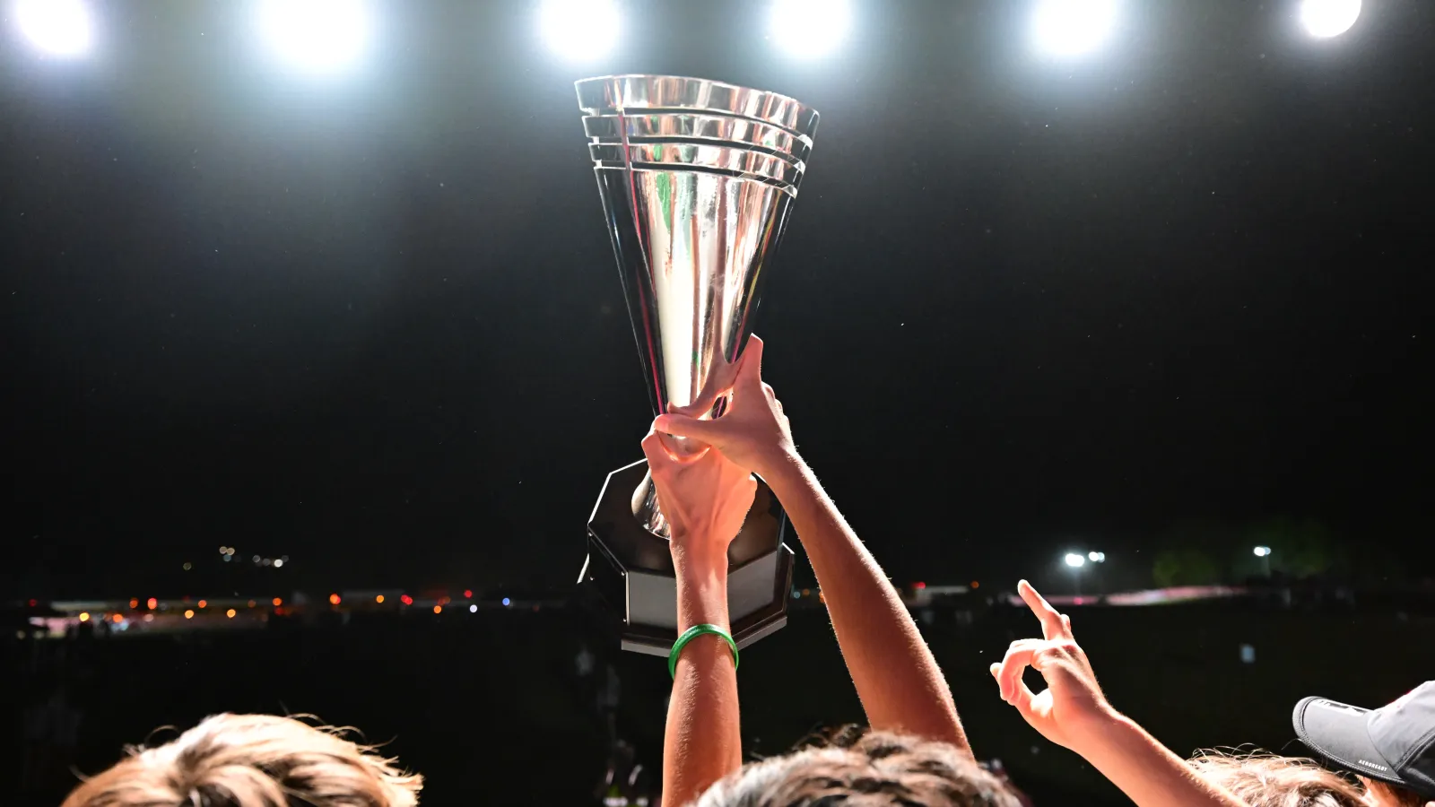 Athletes lift a large silver trophy under bright stadium lights during a nighttime celebration.
