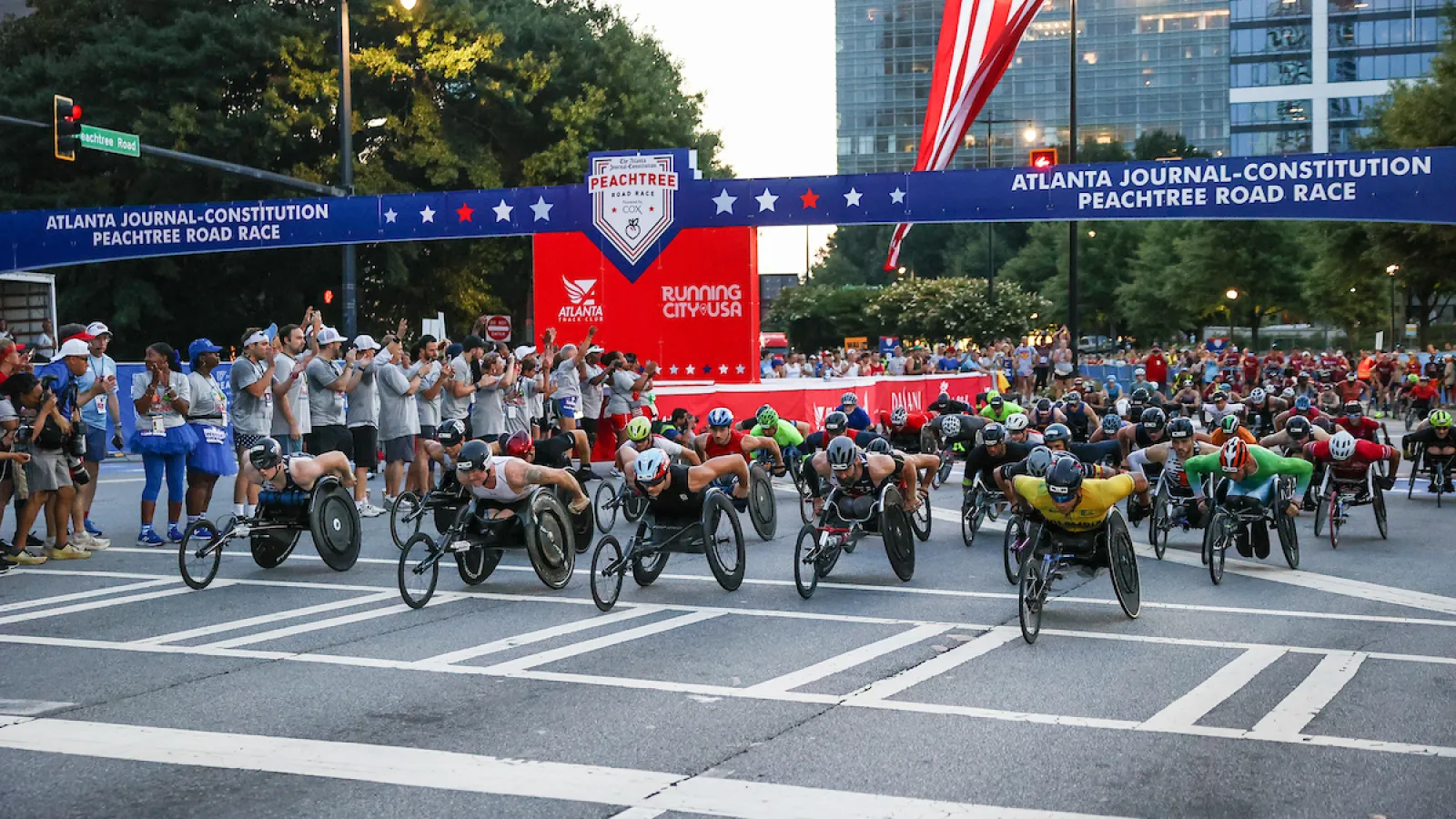 Athletes in wheelchairs race at the start of the Atlanta Journal-Constitution Peachtree Road Race with spectators cheering.
