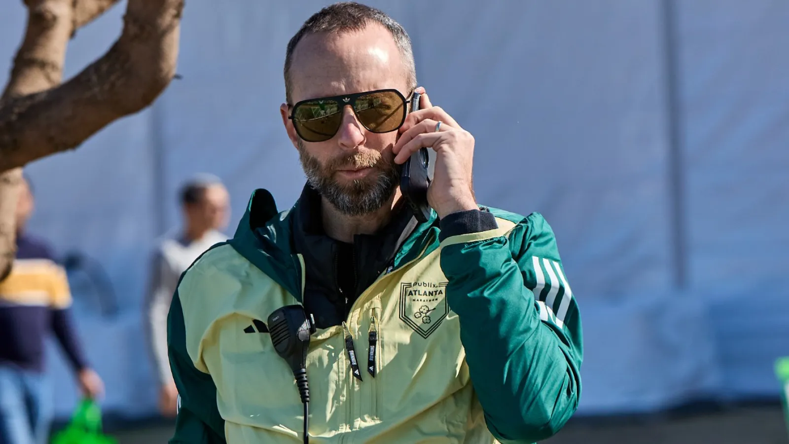 Man in sports jacket and sunglasses using a walkie-talkie outside on a sunny day