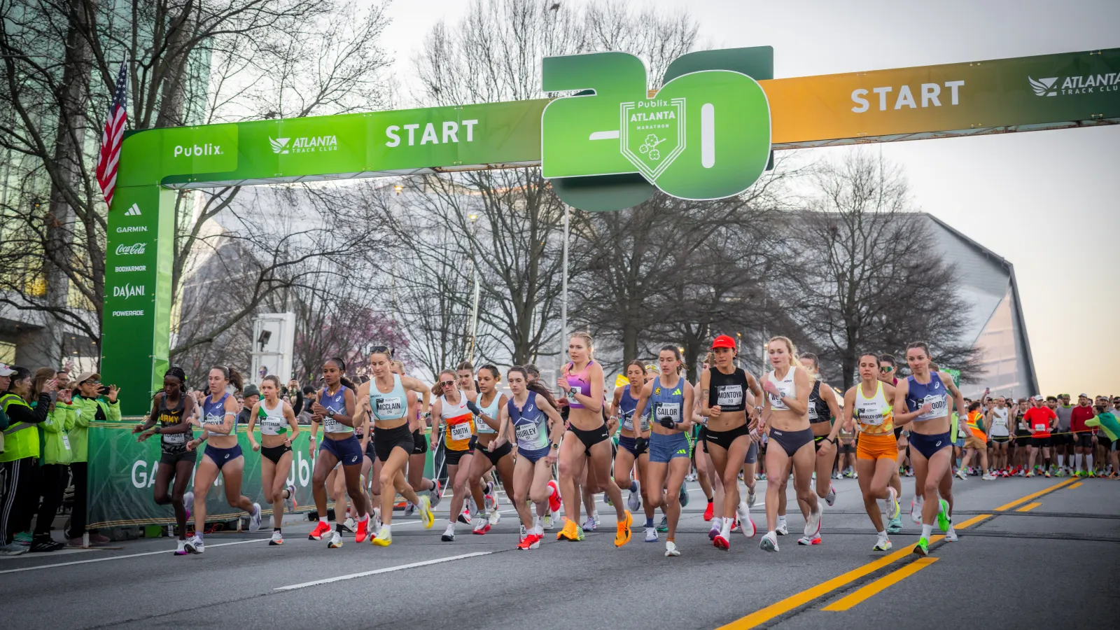Women runners start the 26th annual Publix Atlanta Track Club race under a green and orange starting arch.