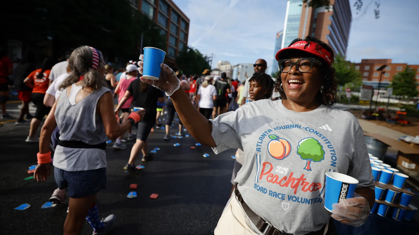 Volunteer offering water to runners at the 2021 Peachtree Road Race in Atlanta on a sunny day.