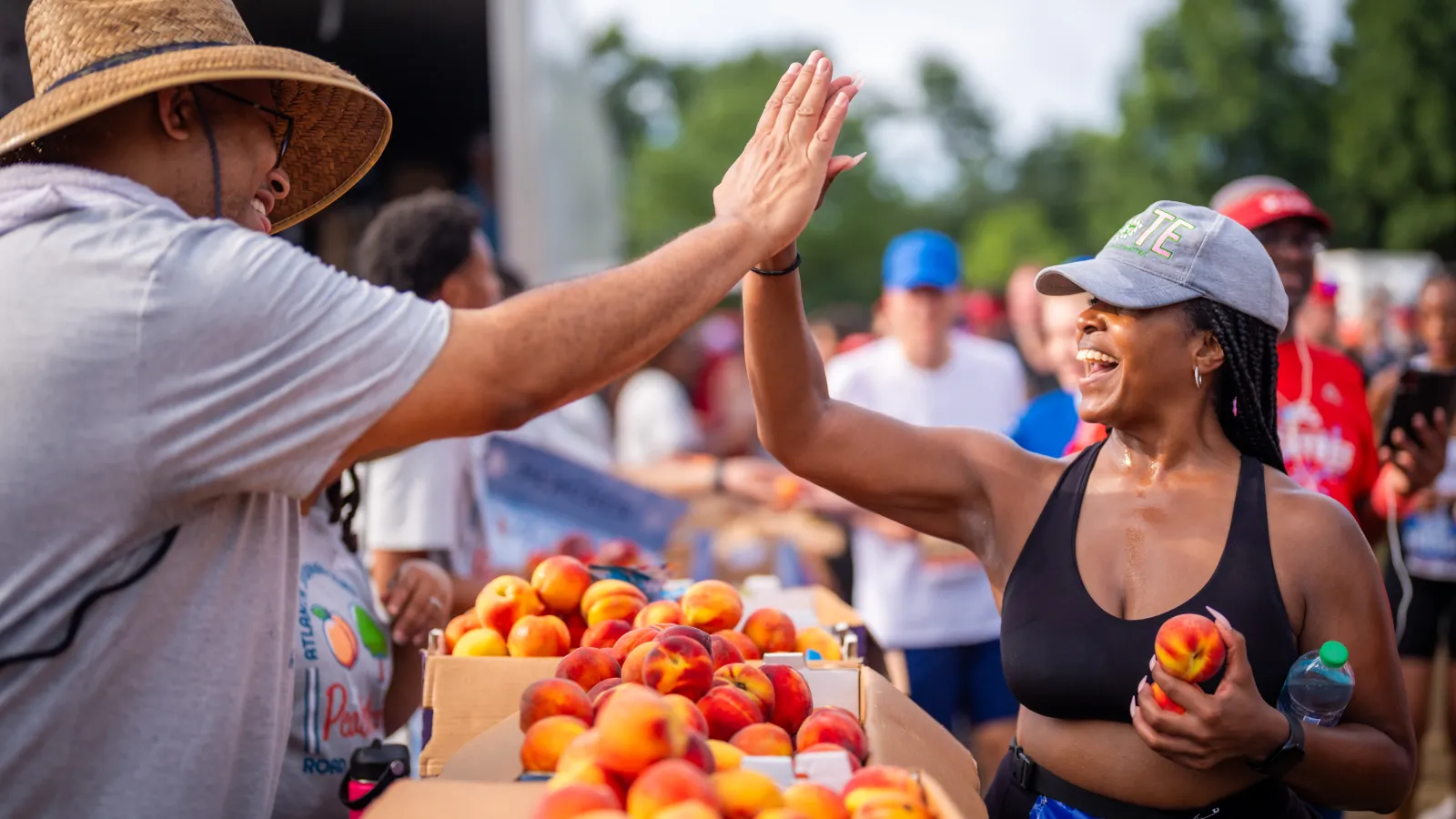 Two people high-fiving at an outdoor peach stand during a community event on a sunny day