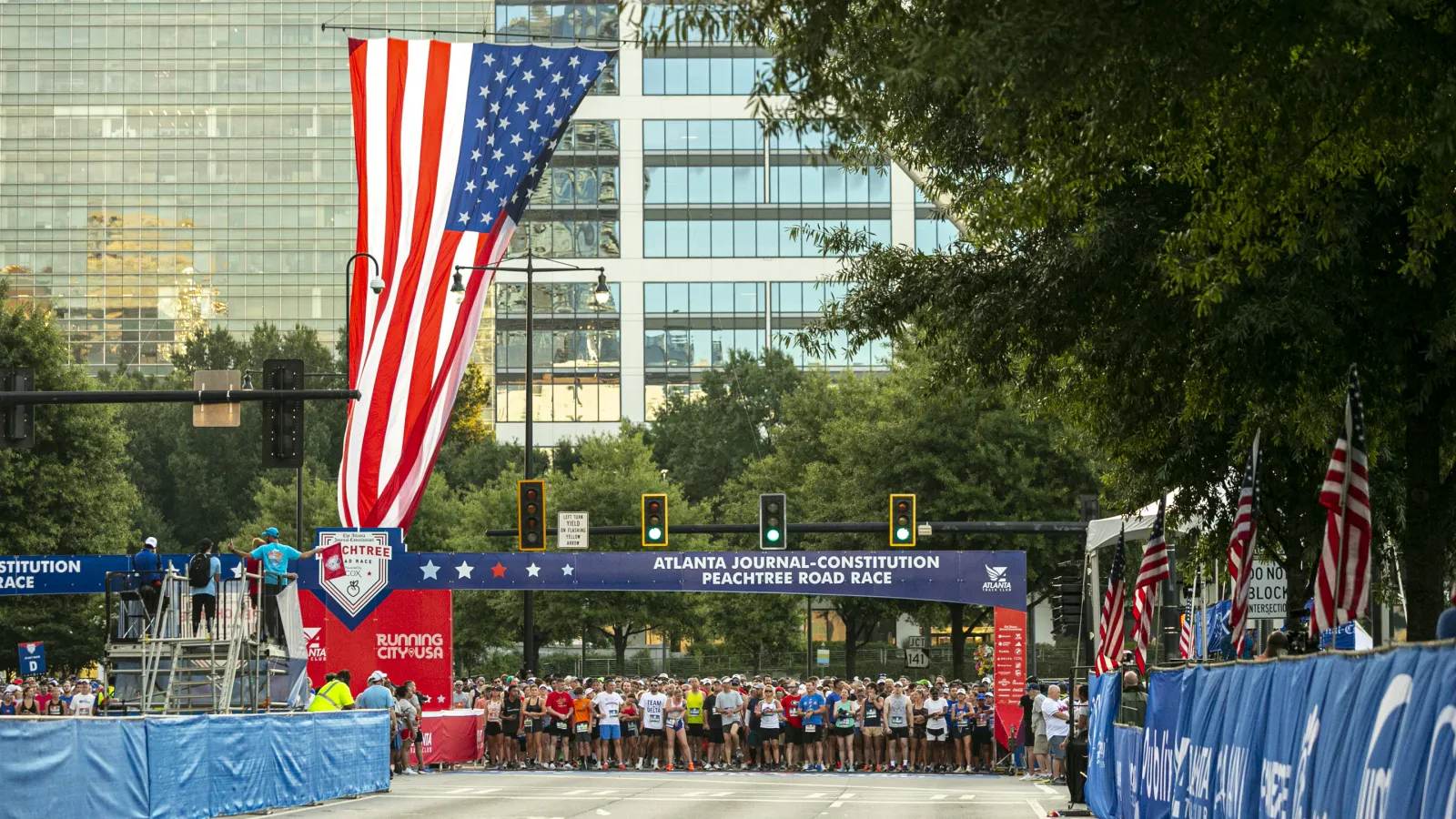 Runners gather at the start line of the Atlanta Journal-Constitution Peachtree Road Race under a large American flag.