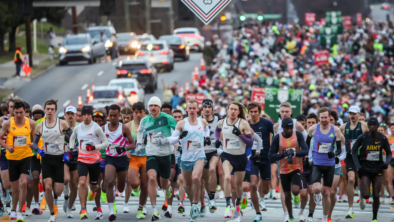 Runners start a marathon race under a green Marathon Weekend banner, with a large crowd behind them.