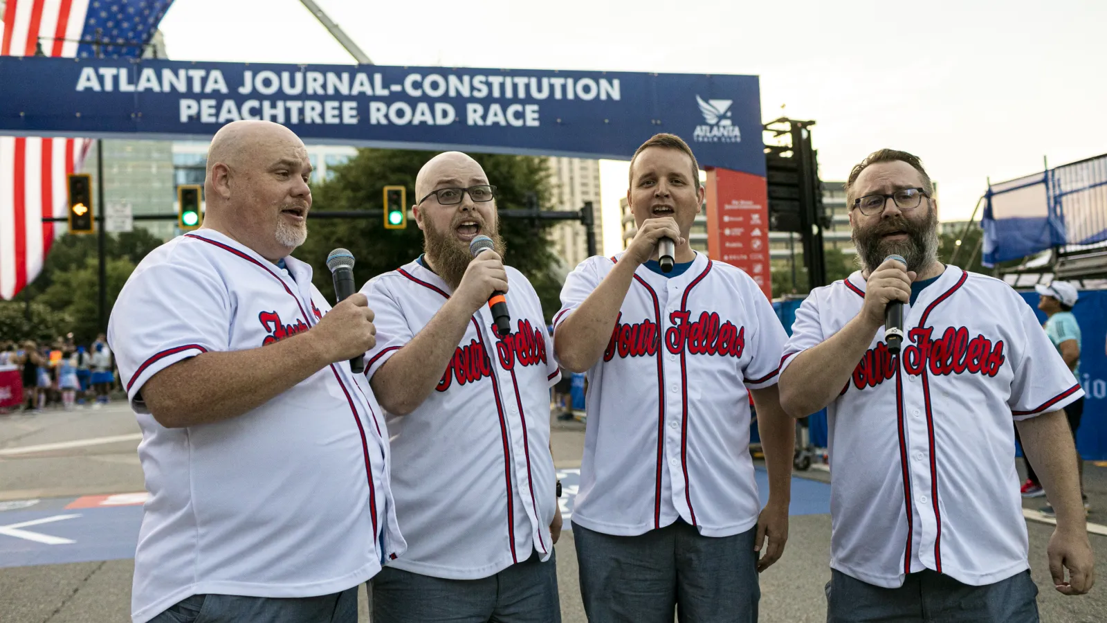Four men in matching jerseys singing with microphones at Atlanta Journal-Constitution Peachtree Road Race event