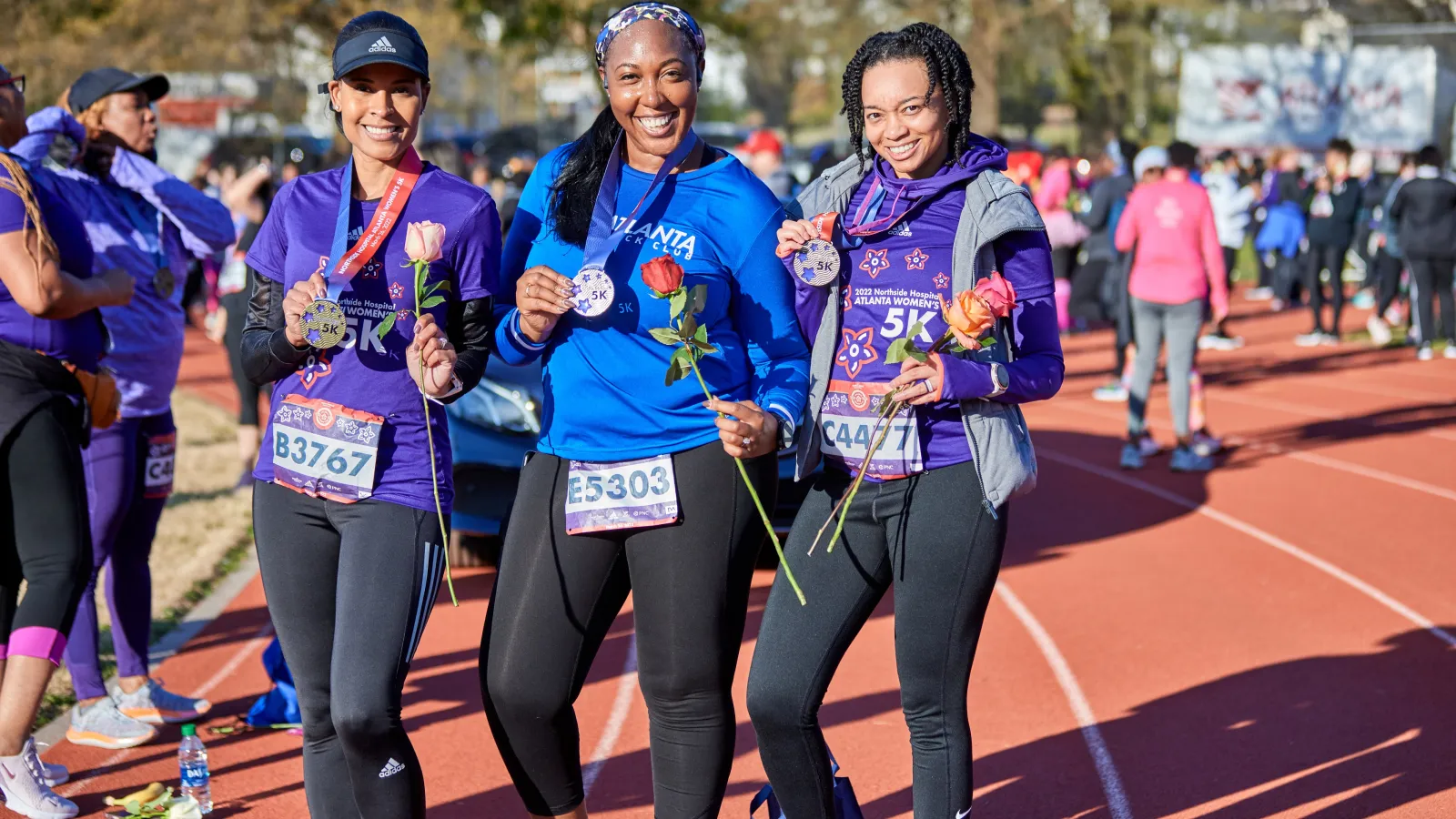 Three women pose for a photo on the track of Cheney Stadium after the 2022 Northside Hospital Atlanta Women's 5K, all holding their 5K medal and a rose. Photo by Paul McPherson.
