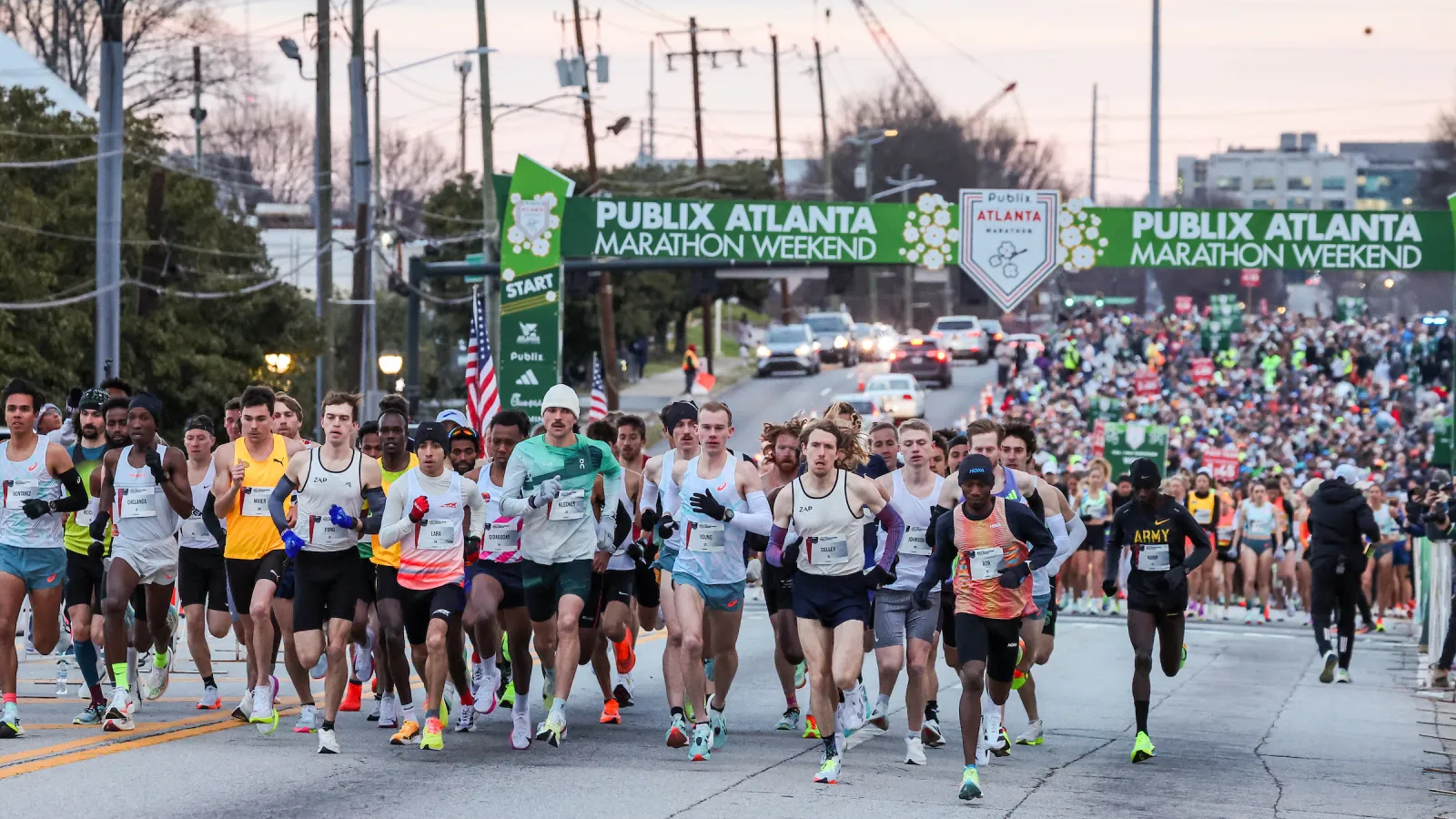 Runners start the Publix Atlanta Marathon Weekend race on city street under green event banners at dawn.