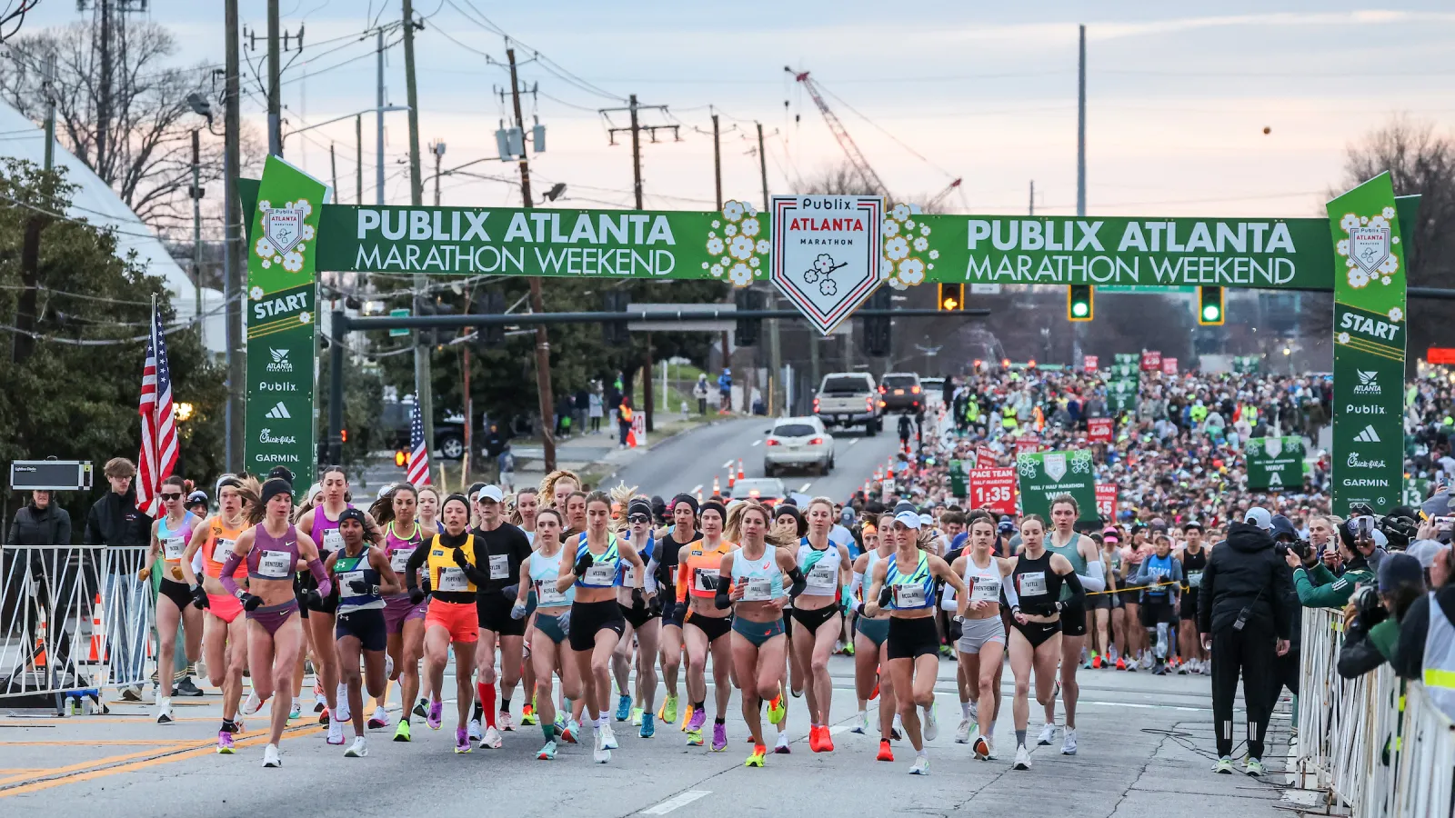 Runners start the Publix Atlanta Marathon Weekend race under green banners on a city street at dawn.
