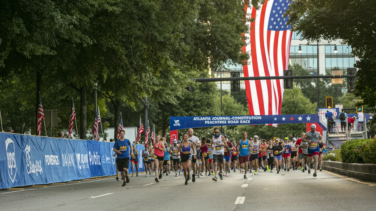 Runners competing in the Atlanta Journal-Constitution Peachtree Road Race under a large American flag