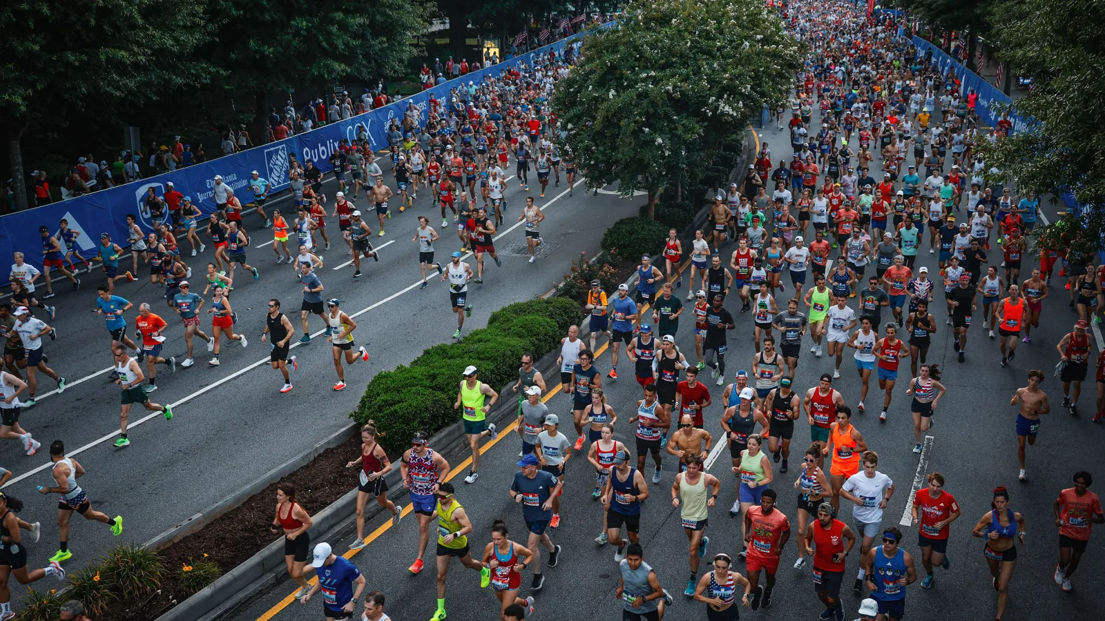 Large group of diverse runners participating in a marathon on a city street lined with trees and barriers.