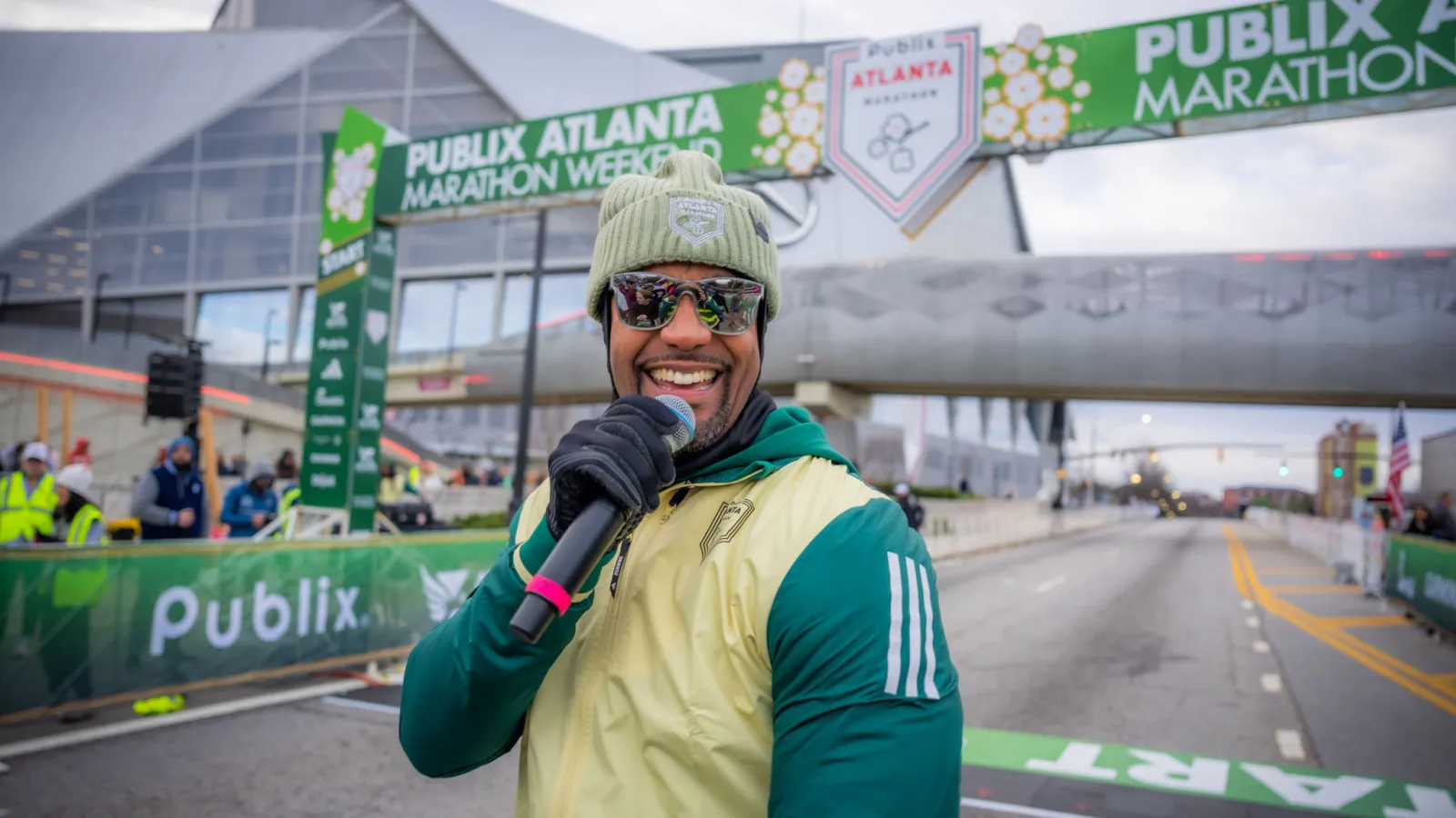 Host smiling with microphone at Publix Atlanta Marathon starting line event in cold weather.