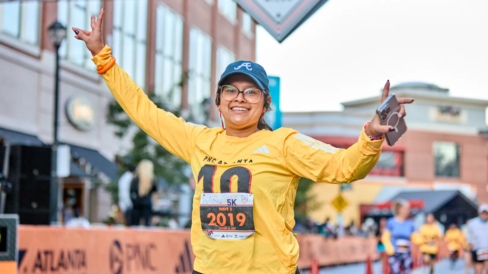 Smiling female runner in yellow shirt and Atlanta cap celebrating during a 5K race in the city streets.