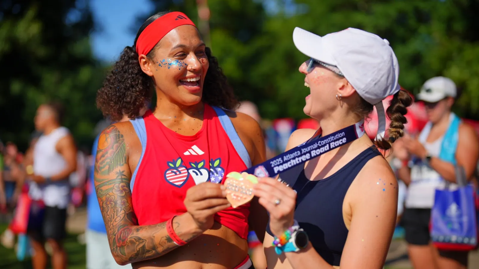 Two women smiling and celebrating with a finisher medal at the 2023 Peachtree Road Race outdoors.