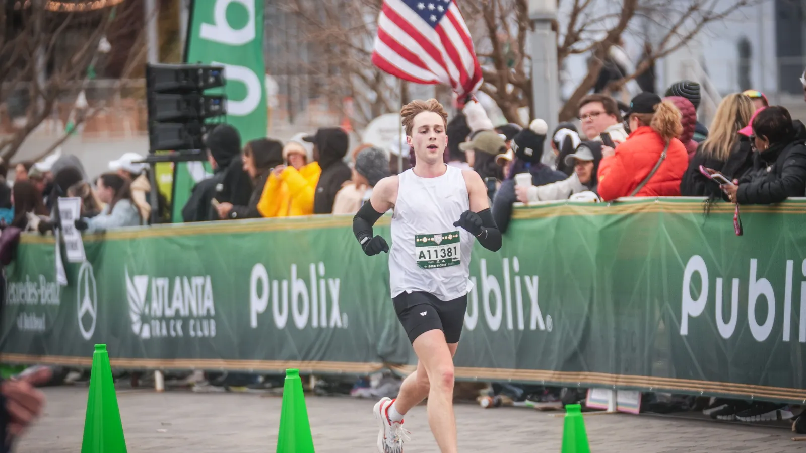 Runner crossing finish line at event with spectators and American flag in background.