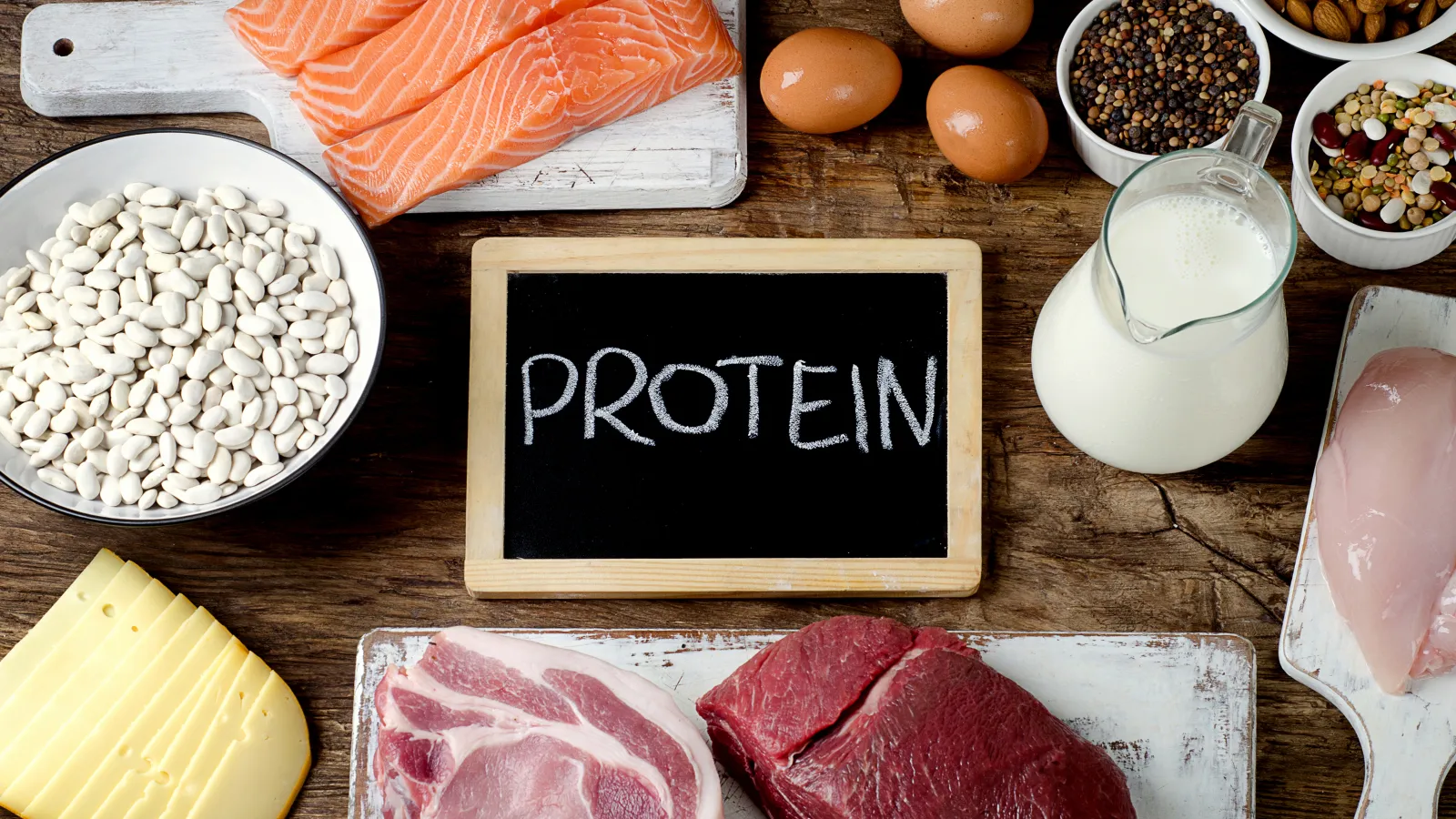 a table full of food with a chalkboard that has the word "PROTEIN" written on it in the center.