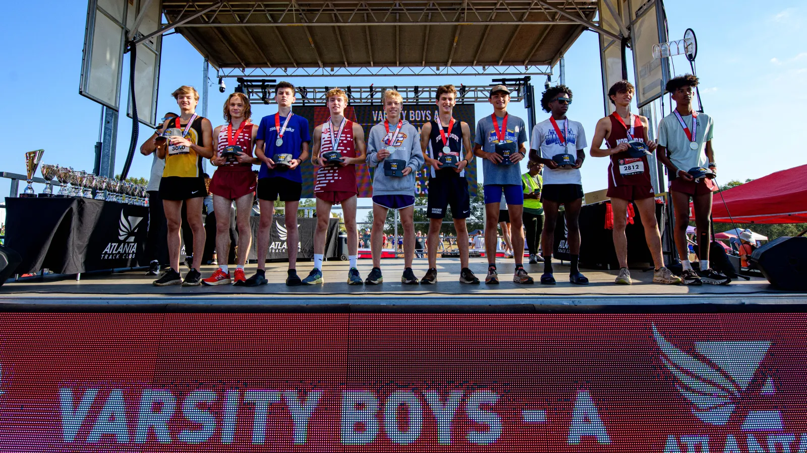 Varsity boys cross-country runners stand on stage holding awards during Atlanta Track Club event.