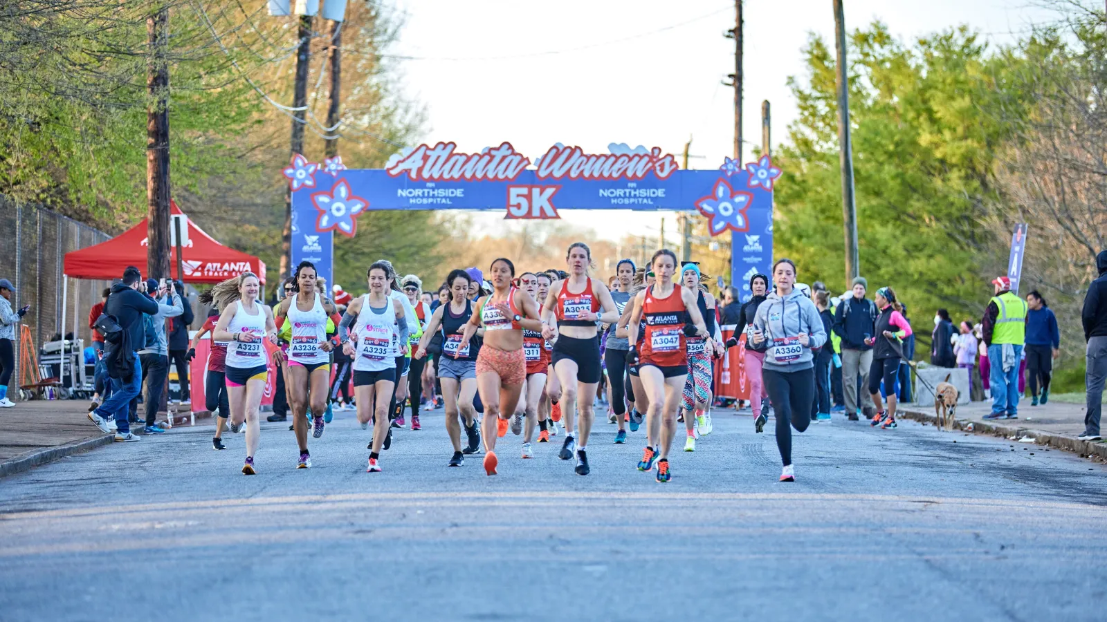 A group of women run past the start line of the 2022 Northside Hospital Atlanta Women's 5K with the start line truss behind them. Photo by Paul McPherson.