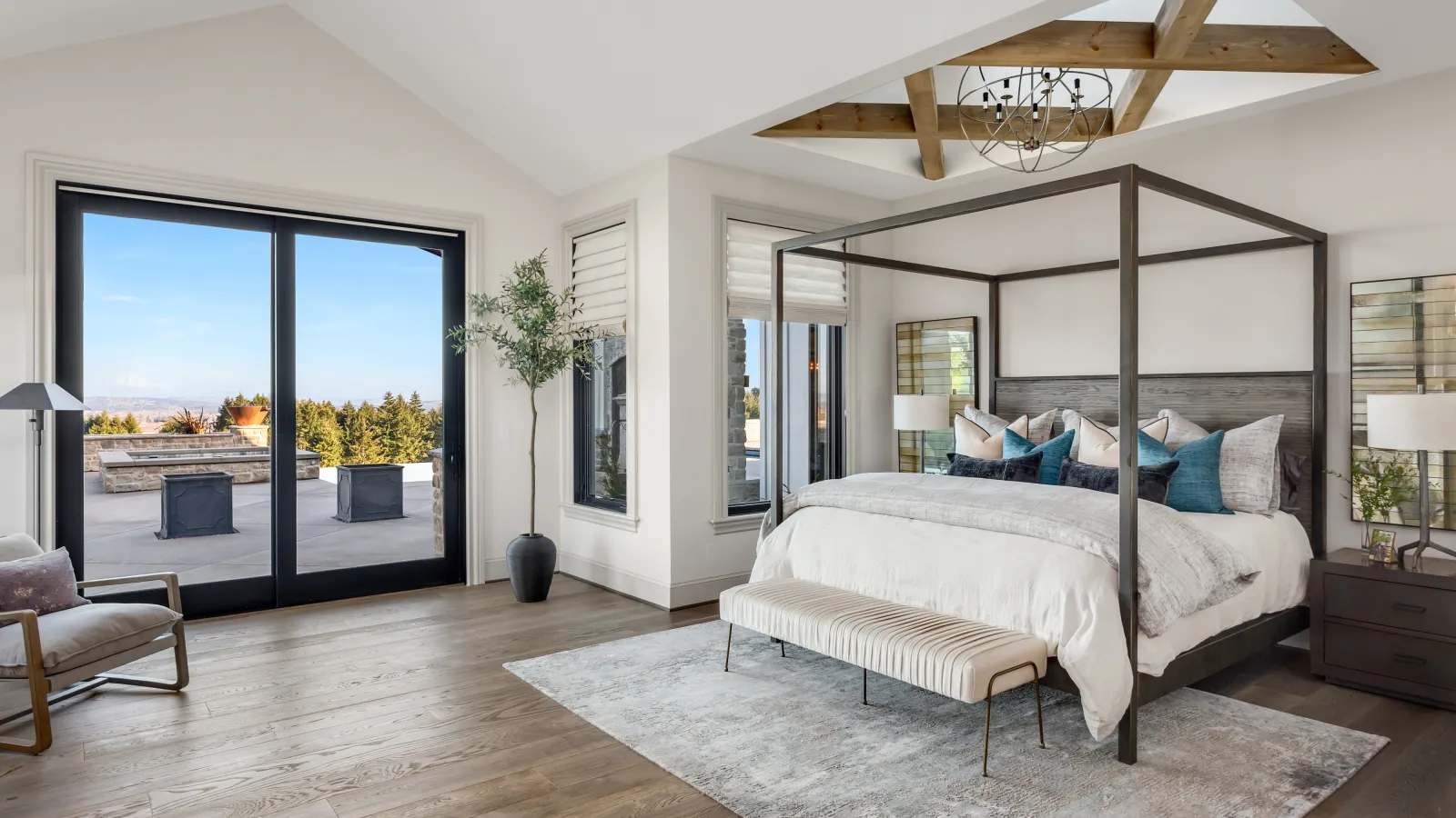 Spacious modern bedroom with a four-poster bed, wooden floors, vaulted ceiling, and large glass doors opening to a patio.