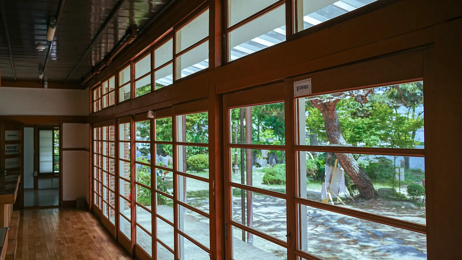 Interior of a traditional Japanese building with wooden floors and large shoji-style windows overlooking a garden.